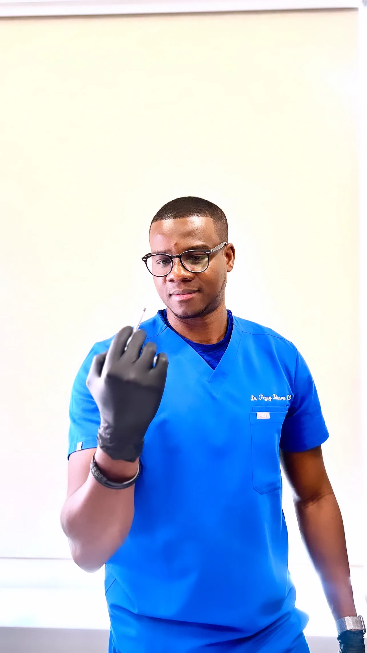 Dr Peguy Télusma, MD, portrait en sarrau bleu tenant un instrument médical, GLIF Medical
